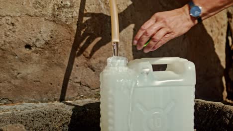 Person-pouring-water-into-plastic-tank-using-outdoor-dispenser,-static-close-up-view