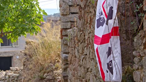 Flag-of-Sardinia-on-side-of-stone-wall-in-small-town,-handheld-view