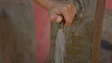 Person-using-outdoor-water-dispenser-on-stone-wall,-close-up-view