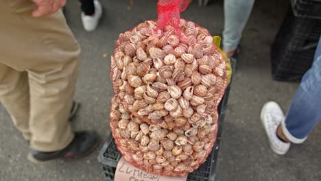 Huge-plastic-net-bag-of-shellfish-in-local-market,-close-up-motion-shot
