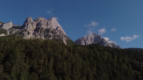 Drone-rising-up-over-woods-in-the-Alps-of-Austria-filming-the-mountain-peaks-with-blue-skies