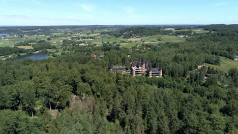 Castle-of-Lapalice-surrounded-by-dense-forest-and-small-villages,-high-altitude-drone-shot