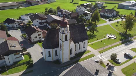 Großartige-Kreisende-Aufnahmen-Einer-Drohne-In-Den-Alpen,-Die-Um-Eine-Wunderschöne-Kirche-Mit-Traditionellen-Häusern-In-Einem-Dorf-Im-Hinteren-Teil-Europas-Herumfliegt