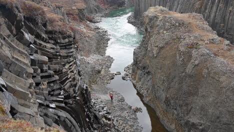 A-person-walking-by-the-river-in-a-canyon-with-grey-basalt-columns
