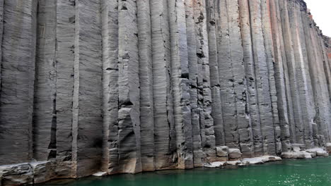 High-grey-basalt-columns-with-dots-of-orange-in-a-canyon-with-green-river