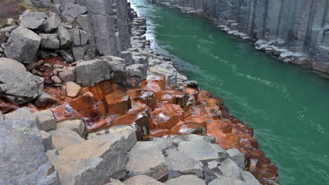 Reveal-of-orange-grey-basalt-canyon-with-a-green-massive-river-flowing-between-steep-rocky-columns