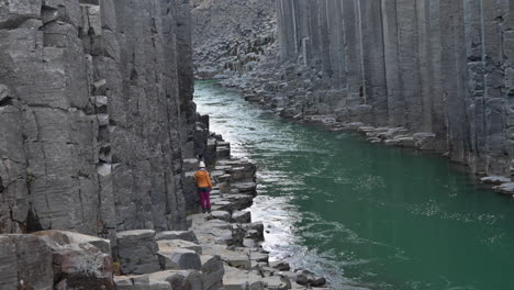 A-person-walking-and-looking-around-on-basalt-rocks-in-a-canyon-with-green-river-and-basalt-columns