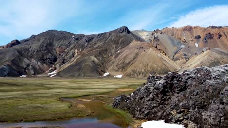 Black-magma-rocks-reveal-a-green-valley-with-patches-of-snow-and-colorful-rainbow-mountains-of-Landmannalaugar-in-Iceland