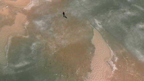 Aerial-high-overhead-of-a-young-girl-walking-on-a-desolate-landscape-by-the-great-salt-lake