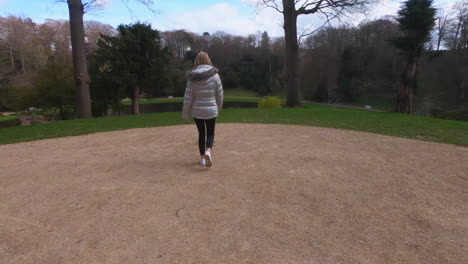 blonde-pretty-woman-walks-dog-in-the-park-in-silver-puffer-coat
