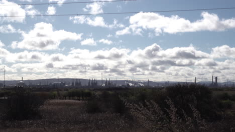 Smoke-rises-from-chimneys-of-a-refinery-in-the-distance-as-clouds-pass-overhead