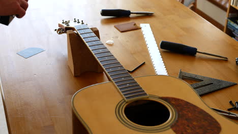 Close-up-hands-of-a-luthier-sanding-and-leveling-the-frets-on-an-acoustic-guitar-neck-fretboard-on-a-wood-workbench-with-lutherie-tools