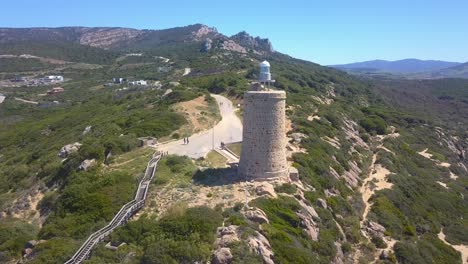 Aerial-shot-of-a-lighthouse-in-the-coast-of-Cadiz,-south-of-Spain,-with-a-walkway-and-the-mountains-behind-on-a-sunny-day