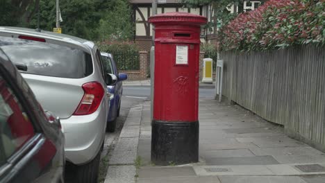 A-Red-Royal-Mail-Post-box-with-a-Royal-Mail-car-passing-by-on-a-residential-road-in-South-West-London