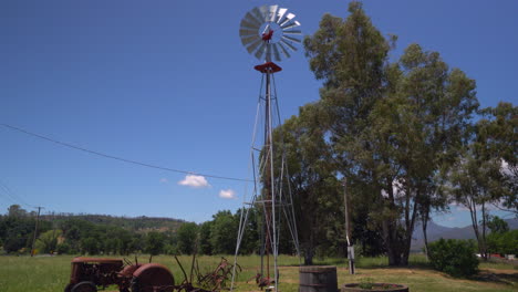 Pan-down-of-a-rustic-windmill-beside-a-vintage-tractor-and-wine-barrel-flower-planters-on-a-farm-in-Northern-California