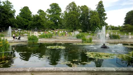 Kensington-Gardens-in-bloom-and-showing-ponds-and-fountains,-along-with-visitors-on-a-sunny-day,-London,-UK