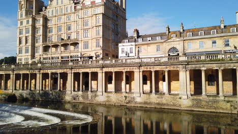 Right-to-Left-Pan-Shot-of-Pulteney-Weir-and-the-Empire-Hotel-in-Bath,-Somerset-on-a-Beautiful-Summer’s-Morning-with-Clear-Blue-Sky