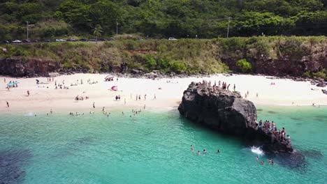 Drone-Shot-moving-towards-a-group-of-people-cliff-jumping-off-of-the-Rock-at-Waimea-Bay,-Pupukea,-Hawaii