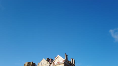 Pulteney-Wehr-Und-Das-Empire-Hotel-In-Bath,-Somerset-An-Einem-Schönen-Sommermorgen,-Der-Diagonal-Vom-Klaren-Blauen-Himmel-Einblendet,-Während-Die-Möwe-In-Zeitlupe-über-Den-Rahmen-Fliegt