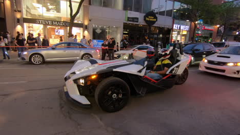Editorial,-view-of-modern-new-Polaris-Slingshot,-a-three-wheeled-motor-vehicle-in-the-street,-with-2-passengers-sitting-in,-driving-in-traffic-and-wearing-helmets