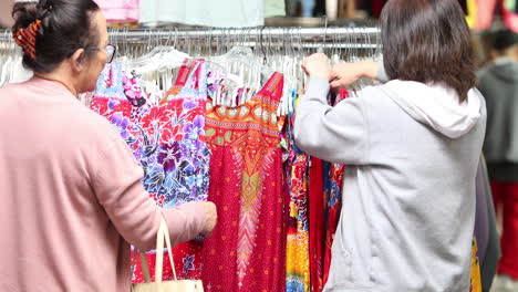 Zwei-Frauen,-Die-Auf-Einem-Outdoor-Markt-Oder-Flohmarkt-In-Chinatown-Durch-Ein-Regal-Mit-Bunten-Kleidern-Schauen