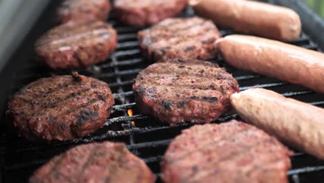 Close-up-footage-panning-over-alternative-meat-burger-patties-and-sausages-on-barbecue-with-flames-as-the-lid-closes,-shot-in-slow-motion-4k