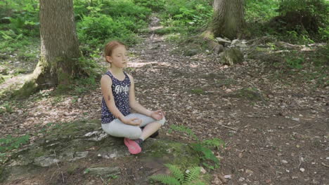 Little-girl-with-red-hair-meditates-in-the-woods,-slow-motion