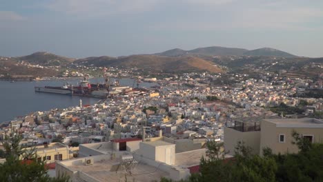 Barrido-Panorámico-Derecho-En-Movimiento-Lento-Sobre-La-Ciudad-De-Syros-Al-Atardecer-Desde-Lo-Alto-Con-Colinas-Y-Montañas-En-La-Distancia