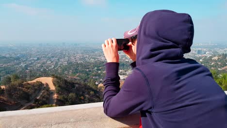Young-woman-taking-a-picture-of-LA-from-the-Griffith-Observatory-with-her-phone-on-a-sunny-and-hazy-day