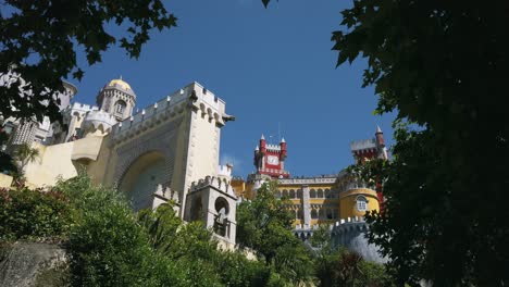 Beautiful-view-through-trees-to-clock-tower-of-colorful-Pena-Palace-on-clear-day-in-Sintra,-Portugal