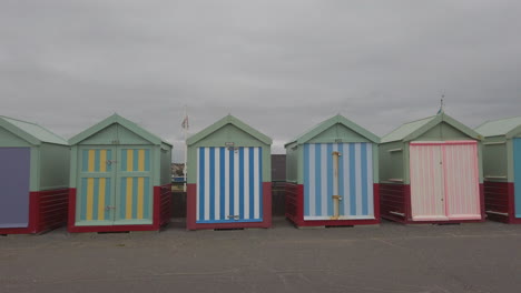 Wide-shot-of-colourful-beach-huts-at-Brighton-beach,-with-a-female-runner-running-past
