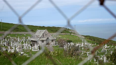 Tudnos-church-Llandudno-coastal-mountain-chapel-cemetery-graveyard-view-through-mesh-fence-dolly-right