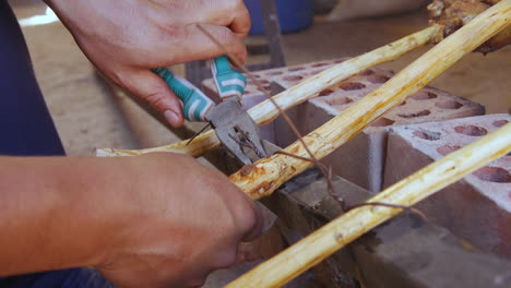 A-close-up-of-a-man's-hands-as-he-uses-pliers-to-tighten-some-wire-around-a-wooden-stick