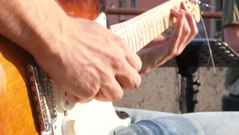 Close-up-of-young-guitar-player-playing-electrical-guitar-on-open-air-concert-on-the-day-of-music,-with-drummer-in-the-background