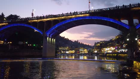 Nach-Sonnenuntergang-Nachtansicht-Der-Straßenbrücke-über-Den-Fluss-Tuo-Jiang-Und-Holzhäuser-In-Der-Alten-Altstadt-Von-Fenghuang,-Bekannt-Als-Phönix