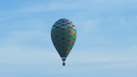 Colorful-hot-air-balloon-floating-in-blue-sky,-bird-flying-trough-the-frame,-medium-distant-shot