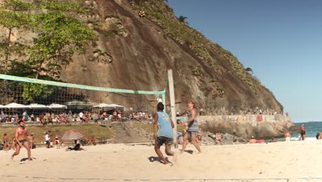 Foot-volleyball-with-volley-net-with-one-woman-and-two-men-playing-in-front-of-the-Leme-hill-at-the-end-of-Copacabana-boulevard-and-kiosks-on-the-edge-of-the-rock