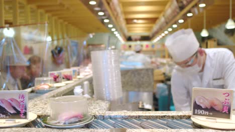 Kaiten-zushi---Chefs-Wearing-Face-Shield-And-Plastic-Sheet-Barrier-Between-Customers,-New-Normal-Scene-In-A-Conveyor-Belt-Sushi-Restaurant-In-Tokyo,-Japan---selective-focus