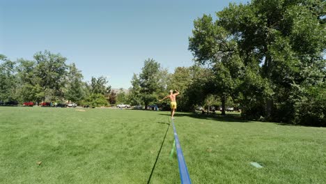 Young-Caucasian-man-balances-himself-on-a-slackline-in-a-park,-as-the-camera-moves-towards-him