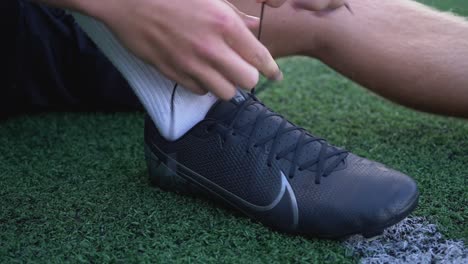 Close-up-of-a-male-soccer-player-tying-shoelace-on-artificial-football-field