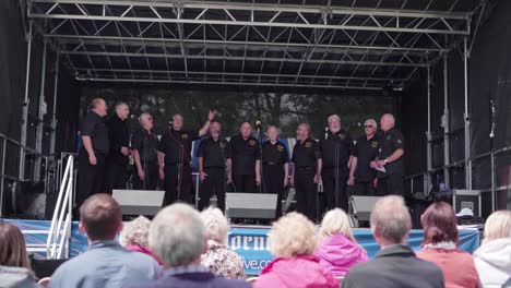 Group-Of-Senior-Men-Singing-On-The-Stage-During-The-Royal-Cornwall-Show-In-Wadebridge,-Cornwall,-England,-UK---View-From-The-Audience---Wide-Shot