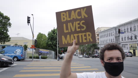 Young-White-Man-in-Mask-Holds-Black-Lives-Matter-Sign-at-Rally,-to-Camera
