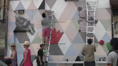 Artistas-En-Escaleras-Pintan-Un-Mural-Callejero-Mientras-Los-Lugareños-Y-Los-Turistas-Caminan