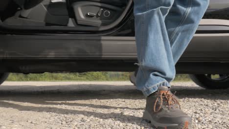 A-young-man-opens-the-door-to-the-vehicle-and-his-feet-can-be-seen-getting-out-of-the-vehicle-and-walking-around-to-the-back-of-the-vehicle