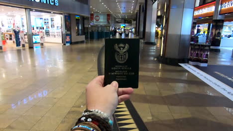 Männliche-Hand,-Die-Einen-Südafrikanischen-Pass-Hält,-Der-Sich-Durch-Einen-Leeren-Flughafen-Bewegt