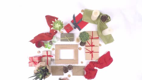 Top-down-view-of-Christmas-decorative-items-on-white-background-with-gift-boxes,-red-ribbons,-small-candles,-pine-cones-and-small-plants