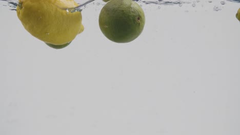 Ganze-Zitronen-Und-Limetten,-Die-In-Wasser-Spritzen