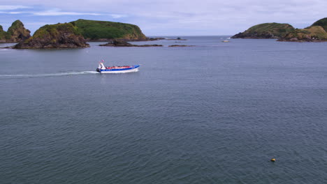Wide-aerial-shot-following-a-tourist-boat-on-the-Chilean-coast-line,-bright-sunny-day