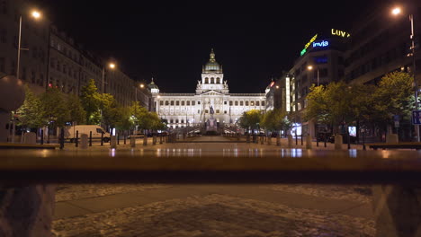 A-view-of-the-National-museum-in-Prague,-Czechia-on-the-empty-Wenceslas-square-in-the-historical-centre,-illuminated-by-street-lamps-during-a-Covid-19-lockdown,-no-people,-pedestal-shot-over-a-bench