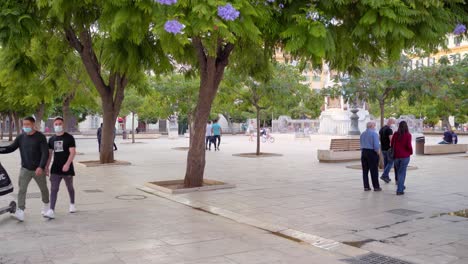 People-Strolling-At-Plaza-de-la-Merced-During-Covid-19-Pandemic-In-Malaga,-Spain---Wearing-Masks-For-Protection---wide-shot